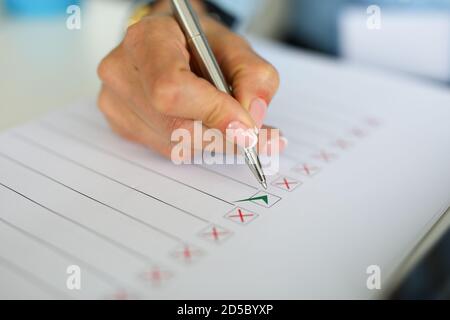 Woman's holding pen on table lies a document with red and green check marks Stock Photo