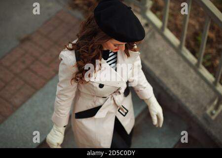 Hello november. Upper view of stylish middle aged woman in beige trench coat walking outdoors on the city street in autumn. Stock Photo