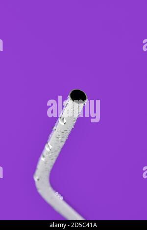 closeup of a wet reusable stainless steel drinking straw on a violet background Stock Photo