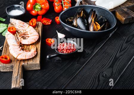 Fresh uncooked sea food specialties and rice with mussels, shrimps and squid on black wooden background with copy space Stock Photo