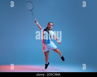 Strong. Beautiful dwarf woman practicing in badminton isolated on blue background in neon light. Lifestyle of inclusive people, diversity and equility. Sport, activity and movement. Copyspace. Stock Photo