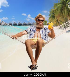 Bearded guy enjoying in a hammock with a cocktail on an exotic beach with water villas in background Stock Photo