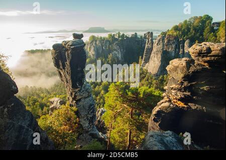 Picuresque  viev over the wehlground to the Bastei bridge with fog in the valley during the sunrise. The distinctive Wehl needle in the foreground. Stock Photo