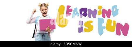 Horizontal crop of excited kid showing yeah while holding laptop near learning is fun lettering on white