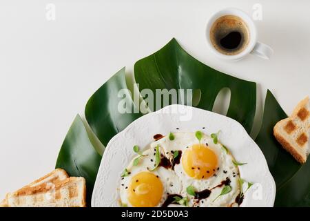 Morning breakfast with fried eggs ,toast and coffee in white cup and plant leaf on white table Stock Photo