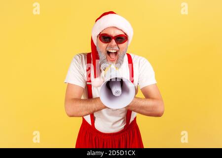 Excited emotional gray bearded man in santa claus costume screaming at loudspeaker, congratulates with holidays, fancy party. Indoor studio shot isola Stock Photo