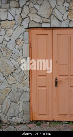 Retro framed wooden door painted in light orange color. Entrance of old building with brick wall faced by rough natural rocks Stock Photo