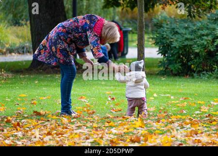 Mother or grandmother playing with kid or child with colorful leaves in a city park in autumn Stock Photo