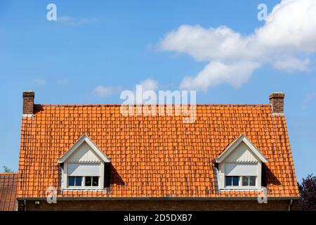 Symmetric red tiled roof with two dormers with rolling shutters and two chimneys in the Netherlands Stock Photo