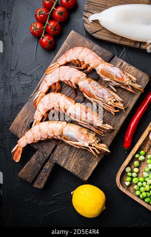 Set of king shrimps with ingredients for paella on black textured background, top view Stock Photo