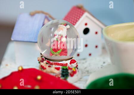 New Year card with blurred bright background of bright bokeh. A snow globe with a snowman santa claus inside is on the table. behind the Christmas Stock Photo