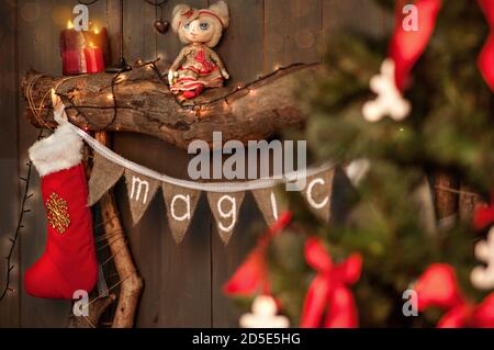 On a wooden fireplace made of old logs, there is a stretch of flags with the inscription Magic, white-red socks for Santa Claus's gifts hang on the Stock Photo