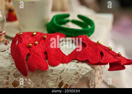 New Year card with blurred background of bright bokeh. Close-up view of a red-green rim. deer ears with bells lying on a vintage tablecloth. Christmas Stock Photo