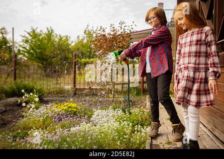 Farmers. Happy brother and sister watering plants in a garden outdoors together. Love, family, lifestyle, harvest, autumn concept. Cheerful, healthy and lovely. Organic food, agriculture, gardening. Stock Photo
