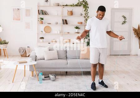 African American Guy Holding Jumping Rope Exercising Standing At Home Stock Photo