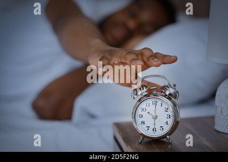 Sleepy African Man Turning Off Alarm-Clock Waking Up At Home Stock Photo