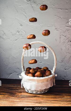 A group of chestnuts falling on a basket full of these fruits. Portrait photography, copy space, autumn concept Stock Photo