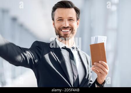 Businessman taking selfie before departure, showing passport with ticket Stock Photo