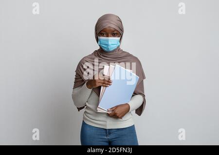 Young black muslim female student in medical mask posing with workbooks Stock Photo