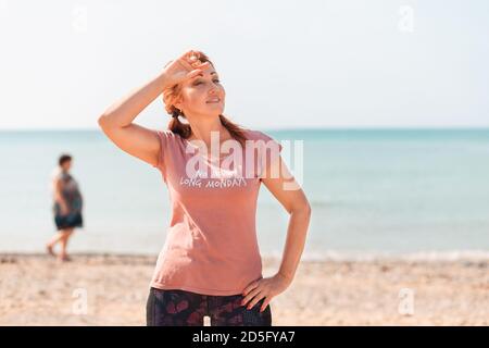 Summer activity. A beautiful adult woman poses on the beach, wiping the sweat from her forehead with her hand, after a workout. Sports lifestyle conce Stock Photo