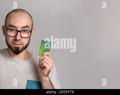 The concept of banking and credit card purchases. A man in glasses smiles and holds a Bank card in his hands. Close up and copy space. Stock Photo
