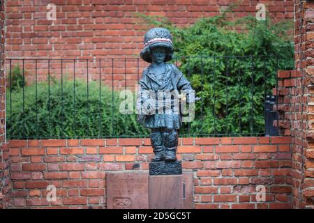 Monument of little boy insurgent in oversized german helmet and boots, participant of Warsaw Uprising in 1944 against red brick of medieval city walls Stock Photo