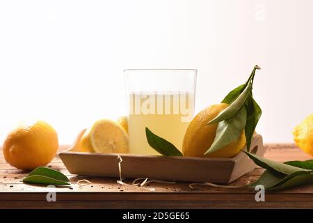 Freshly squeezed juice on a wooden table full of lemons white isolated background. Front view. Horizontal composition. Stock Photo