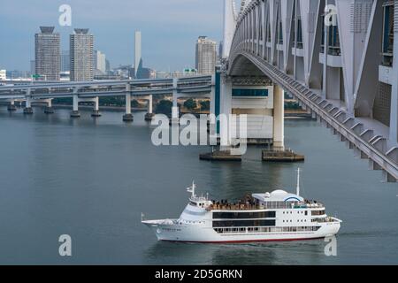 Sightseeing Cruise Ship runs under the Rainbow Bridge on the Tokyo Bay. Stock Photo