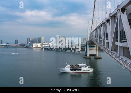 Sightseeing Cruise Ship runs under the Rainbow Bridge on the Tokyo Bay. Stock Photo