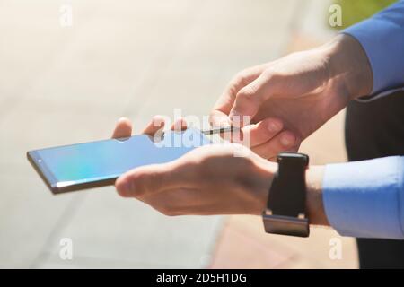 Cropped shot of a businessman using flash drive for smartphone while working outdoors on a sunny day, focus on male hands Stock Photo