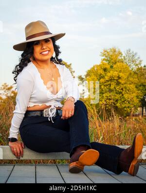 Young Mexican woman is wearing a sombrero and boots while sitting outdoors in autumn Stock Photo