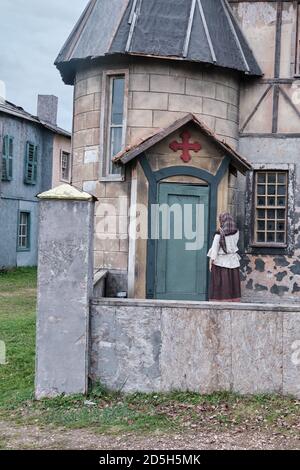 A woman in an old dress in the courtyard of an old catholic Church with a large red cross over the door Stock Photo
