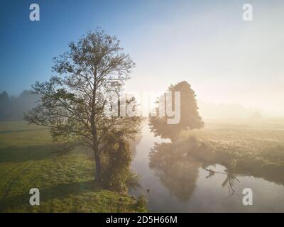 Autumn foggy sunrise. Colorful misty morning dawn. Fall rural scene. Small river with trees in meadow and field, Belarus Stock Photo