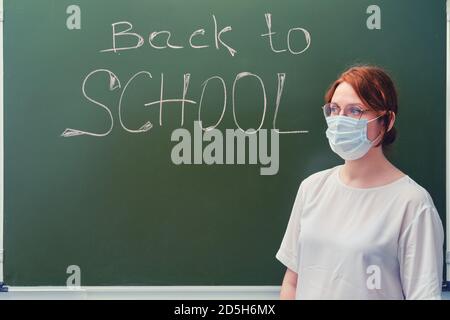 Woman teacher stands next to the text "Back to schoo" on the school blackboard. Problems of school education and Internet lessons in the coronavirus p Stock Photo