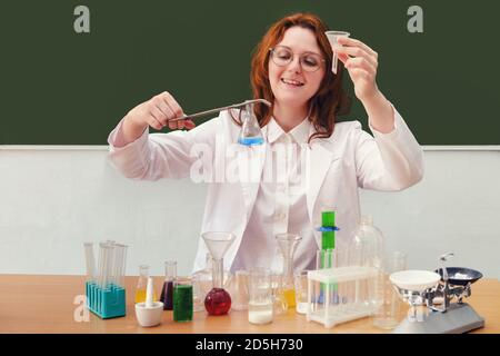 A chemistry teacher holds a bottle in a clip and a funnel for liquid. Woman holds blue reagent in hot bottle with forceps, copy space Stock Photo