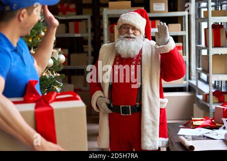 Santa Claus waving hand to courier delivering Christmas present parcel. Stock Photo