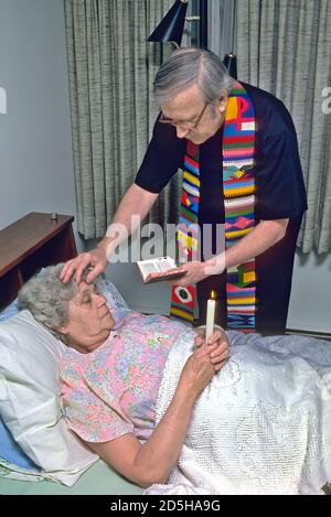 Catholic priest administers last rites to sick elderly female in bed The sacrament of Anointing of the Sick Stock Photo