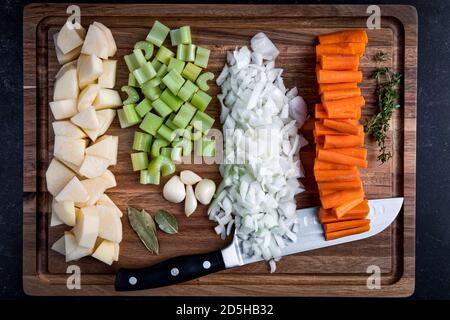 Raw carrots, onions potatoes, celery with garlic, thyme and bay leaves, being prepared to be put into a soup, on a cutting board Stock Photo