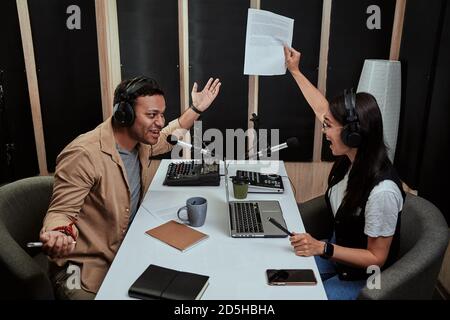 Portait of two radio hosts, young man and woman looking emotional while talking with each other, moderating a live show in studio Stock Photo