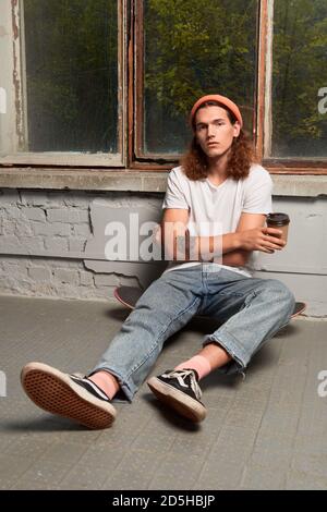 Young adult guy sitting on floor with beverage Stock Photo