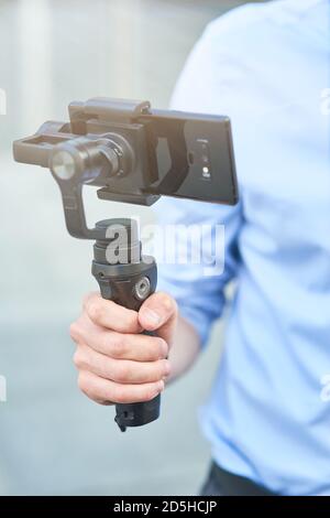 Cropped shot of a male blogger holding a gimbal with smartphone while standing outdoors, recording video for blog, vertical shot Stock Photo