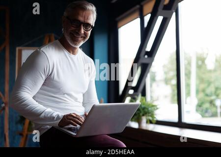 Casual Grey-haired Mature Male business executive using laptop in office. Stock Photo