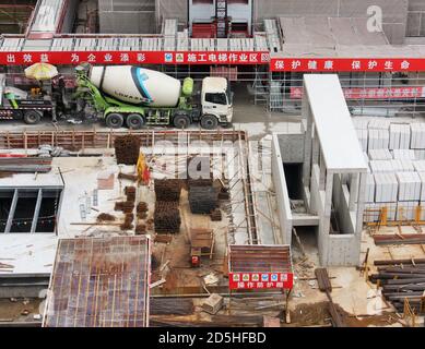 Urban construction site with cement mixers, concrete, scaffolding, building materials, rebar and signs written in Chinese language about worker safety