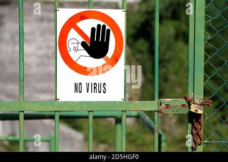 Gate closed with padlock and red sign with large black hand indicating to stop and great message NO VIRUS Stock Photo