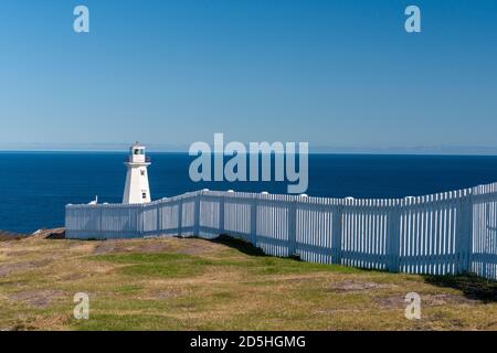 A white circular lighthouse with a green beacon light. The building has multiple windows. Stock Photo