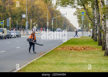 Moscow. Russia. October 11, 2020 A woman utility worker uses a blower to remove fallen leaves on a city street. Technological equipment. Yellow leaves Stock Photo