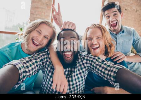 Self-portrait of four nice attractive glad cheerful cheery guys gathering having fun spending time holiday showing v-sign at industrial loft style Stock Photo