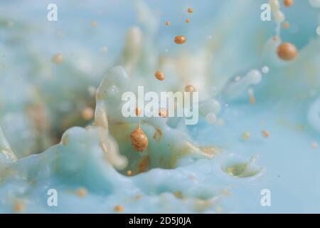 Gold paint splashing into beautiful turquoise paint creating lots of paint bubbles and droplets and other effects. Stock Photo
