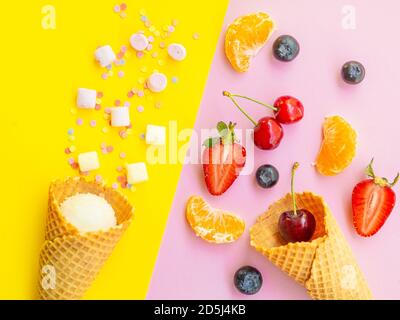 Healthy vs unhealthy dessert, dieting concept. Blueberries strawberries orange cherries on pink vs ice cream sugar sweets isolated on yellow color stu Stock Photo