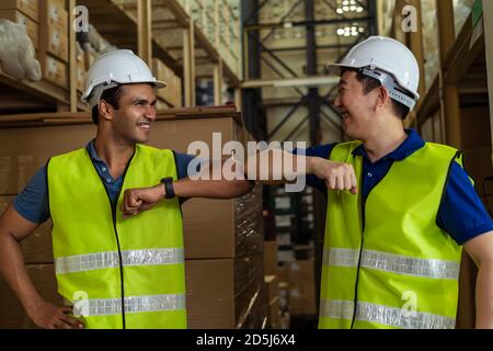 Male factory warehouse workers doing elbow bump working in logistic industry indoor. Friends greeting and shaking with elbows as new normal after Covid-19 Stock Photo